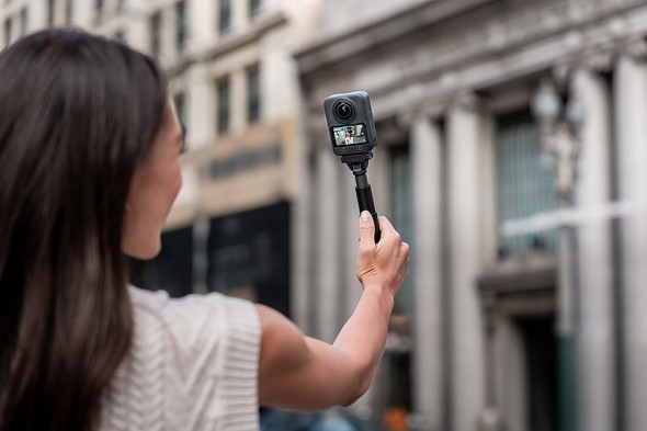 a woman holds out a small action camera on a selfie stick