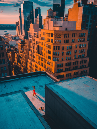 A woman in red standing on a rooftop with the city skyline glowing behind her, highlighting the warm tones typical of golden hour portraits.