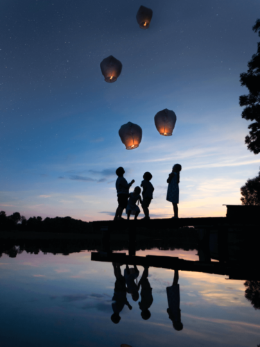 Family silhouette walking together after sunset with lanterns glowing and reflecting on the beach.