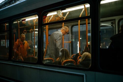 Passengers inside a dimly lit city bus during a Bristol evening commute, with warm orange handrails contrasting against the cool dusk outside, captured by Sirun Tang.