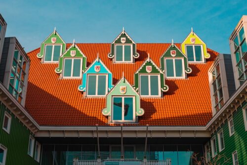 Colorful gabled windows on a red-tiled roof in Zaandam, Netherlands, captured by Sirun Tang, showcasing a whimsical Dutch architectural style.