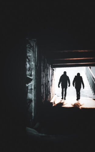 Urban street photography by Nicole Grenier showing two silhouetted figures walking through a dark underpass toward the light.