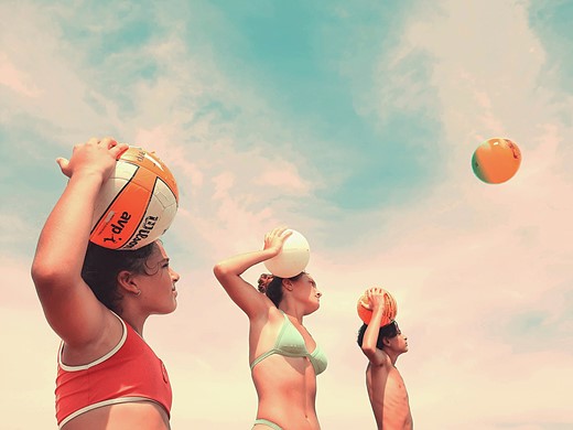 three people stand holding balls to their heads with whispy clouds above them