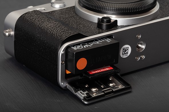 a black and silver camera has the battery and sd card popped out while on a black table