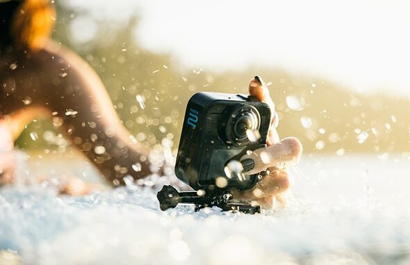 a_hand_holds_the_gopro_max_2_camera_while_water_splashes_around_it