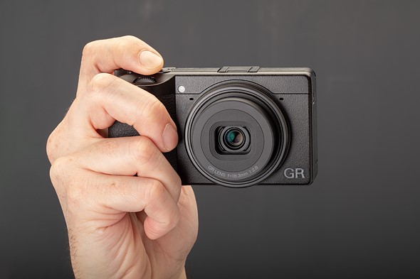 a hand holds the ricoh gr iv compact camera in front a black background