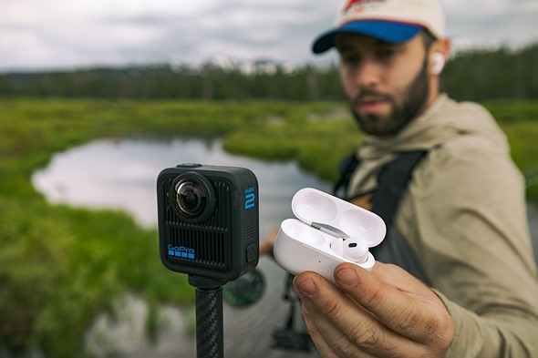 a man holds apple airpods next to the gopro max 2 camera while flyfishing