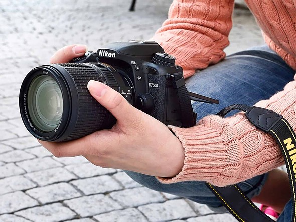 a person squats on a cobble patio while holding the nikon d7500
