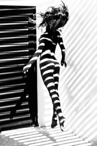Black and white photo by Olena Leliuk of a woman in motion, her body covered in dramatic striped shadows, creating an abstract optical effect.