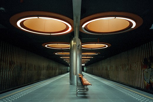Large orange circular lights loom over orange seats in an empty metro station