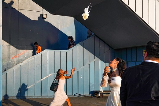 a bride throws her flowers to a woman in a white dress behind her