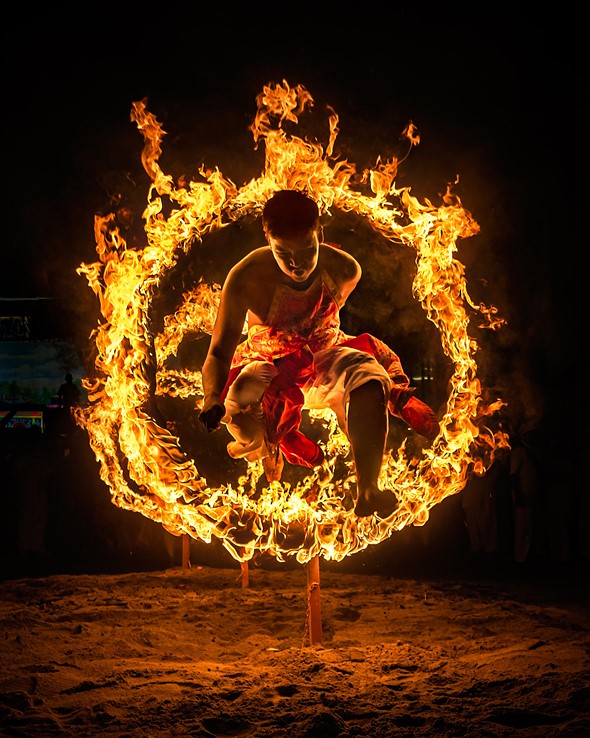 a man jumps through a firey hoop at night