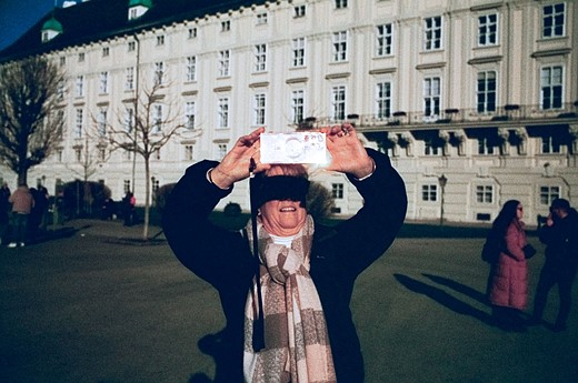 a person holds up their phone to take a picture casting a shadow on their eyes with a large historic building in the background