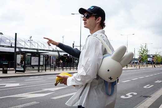 a person with a bunny backpack stands holding bananas on a roadside