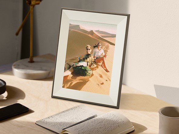 a photo frame sits on a wood desk with a notebook and other items