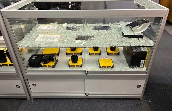 a_shattered_glass_display_case_with_missing_camera_gear_sits_in_a_store
