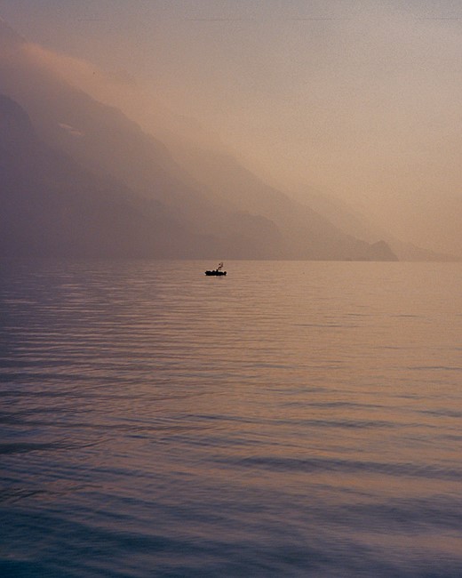 a small boat is in the water with mountains looming in the background and pastel colored light refelcted on the water