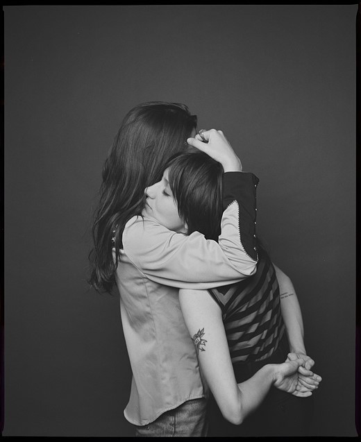 a woman embraces another women who has her hands behind her back