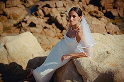 a woman in a slim fitting white wedding dress and veil leans on red rocks
