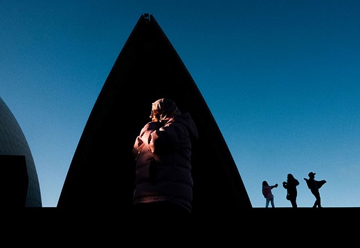 a woman is illuminated by light in front of a triangle shadow with three people in the background