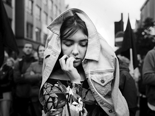 a young girl bites her fingernails with a jean jacket on her head while standing in a crowd