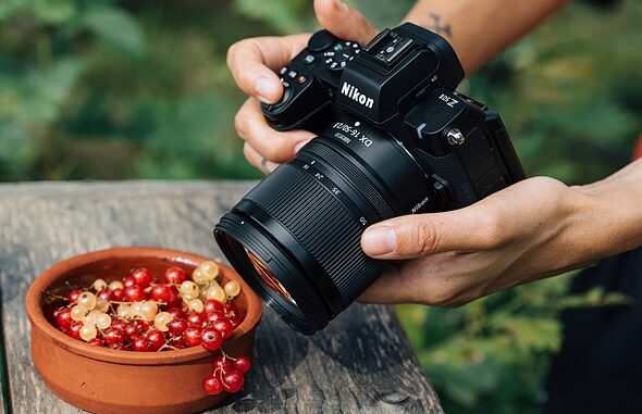 hands_hold_a_nikon_camera_above_a_clay_bowl_of_grapes_on_a_wooden_table