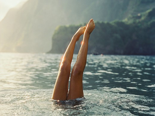 legs stick out of water with tall cliffs in the background