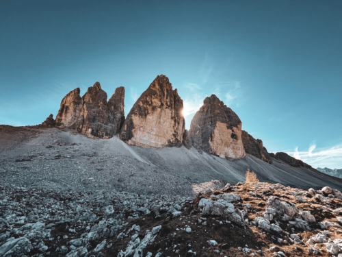 Landscape photo by Andrea Gambirasio capturing the Tre Cime di Lavaredo peaks in the Dolomites with sunlight breaking behind the mountains.