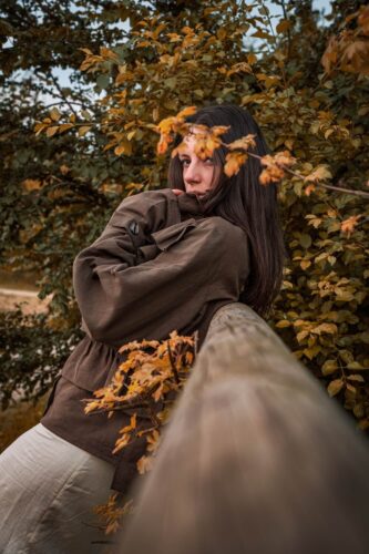 Portrait photo by Andrea Gambirasio of a woman leaning against a wooden fence surrounded by autumn leaves and warm tones.