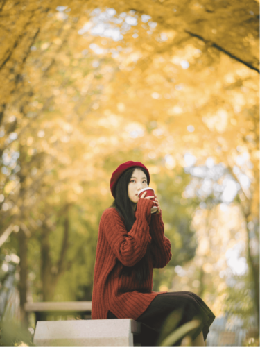 Soulful seasonal portraits of a woman in a red beret sipping coffee under golden autumn trees, bathed in soft seasonal light.