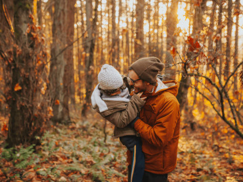 Soulful seasonal portraits capturing a father and child laughing together in a sunlit autumn forest filled with orange leaves.