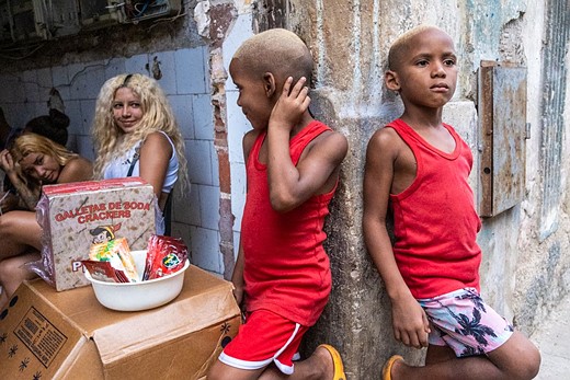 two children in red tanktops stand against a wall next to two women who are seated