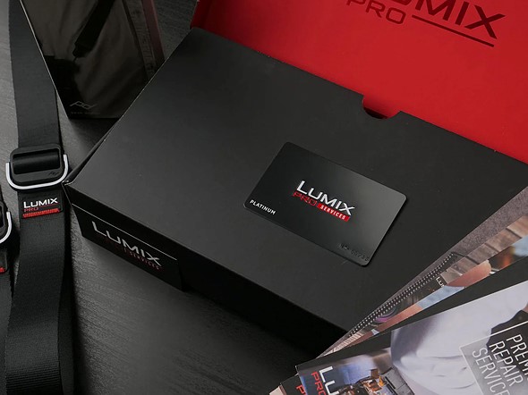 a black and red box with lumix platnimum card inside sits on a black table with other gear and magazines