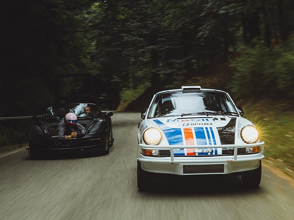 a car with a photographer in the front trunk follows a white orange and blue race Car