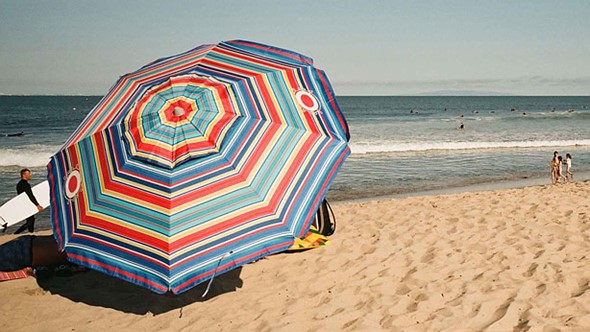 a colorful beach umbrella sits in the sand while people swim in the water in the distance