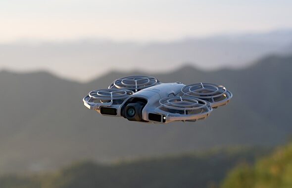 a_drone_hovers_in_the_air_above_a_mountain_vista_with_clear_skies