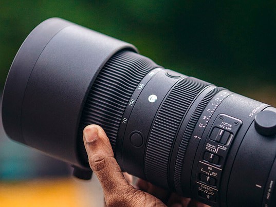 a hand holds a sigma 70-200mm lens in front of a blurred background