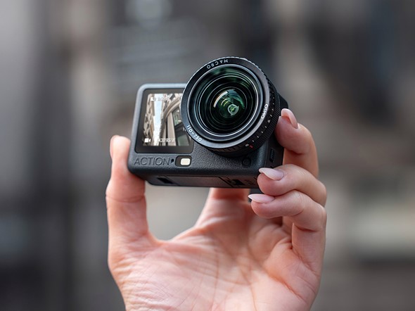 a hand holds the dji osmo action 6 with macro lens mod in front of a blurred background