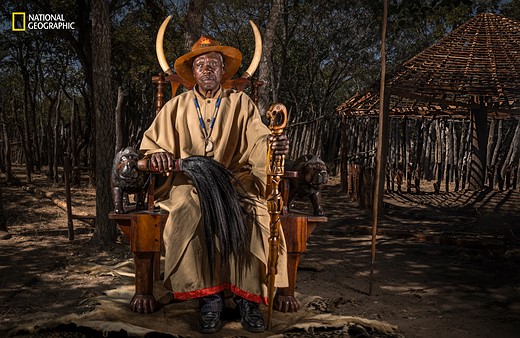 a man in traditional clothing sits on a throne in a forest