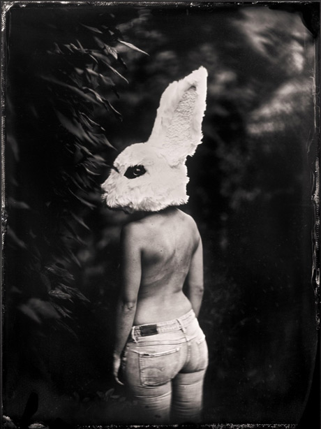 a person with a rabbit head costume on their head stands in front of thick vegitation