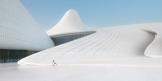 a small child rides a scooter on a white plaza with curved white buildings round