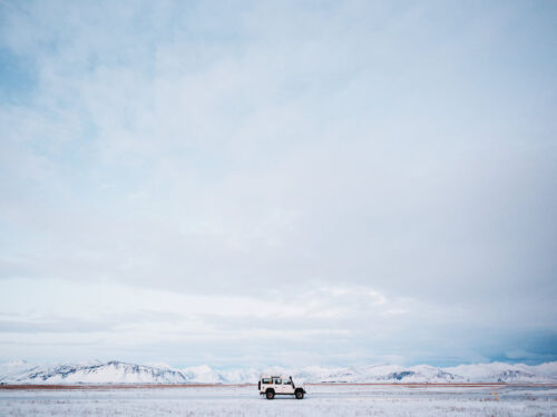 A lone white jeep parked in an expansive snowy field, using framing techniques to highlight scale through a wide sky and distant mountains.