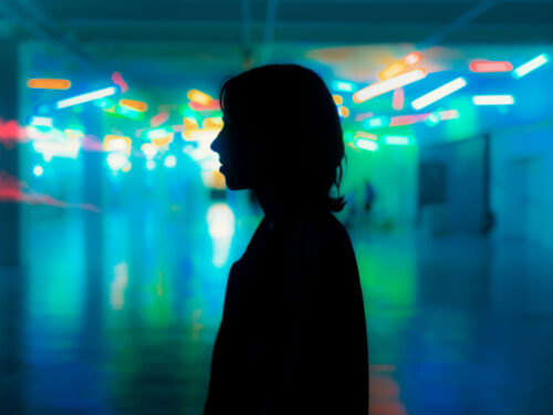 A silhouette of a person standing in a room glowing with neon blue and green lights, using mood editing techniques to create an atmospheric, futuristic feeling.