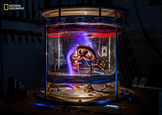 purple light glows inside a glass cylinder filled with wires and special equipment