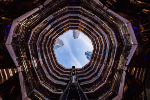 Architectural photo by Marco Tagliarino looking up through the circular interior of The Vessel in New York, framing the sky and surrounding skyscrapers.