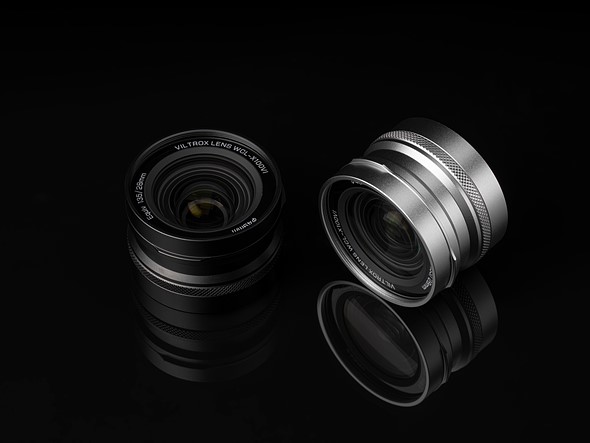 a black and silver viltrox lens are on a reflective black surface with dim lighting