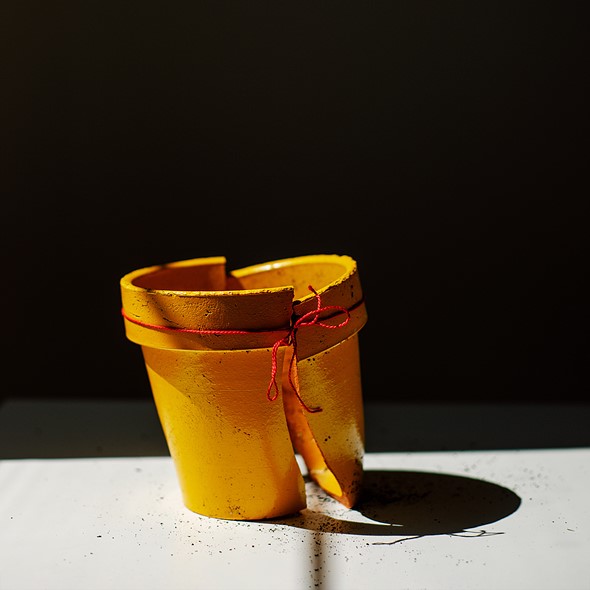 a broken yellow flower pot is hold together with red string with strong light casting shadows