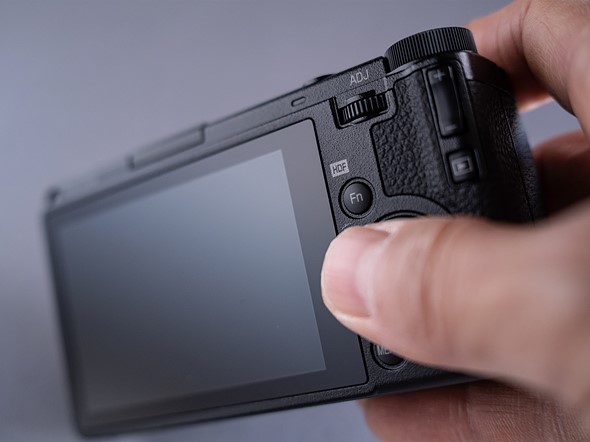 fingers hold a black camera in front of a gray background