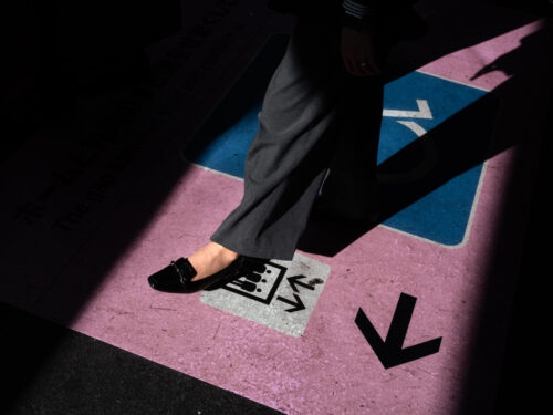 A close-up of a person’s foot stepping onto a painted directional symbol on the ground, using shadow and color to convey choice, movement, and tension in a personal photo essay.