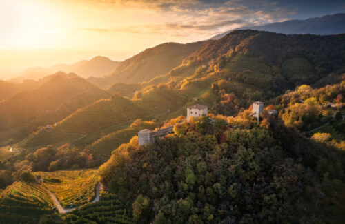 Golden-hour landscape of terraced vineyards and historic stone ruins set among rolling hills, captured during Questmas 2025 by Alberto Agnoletto.